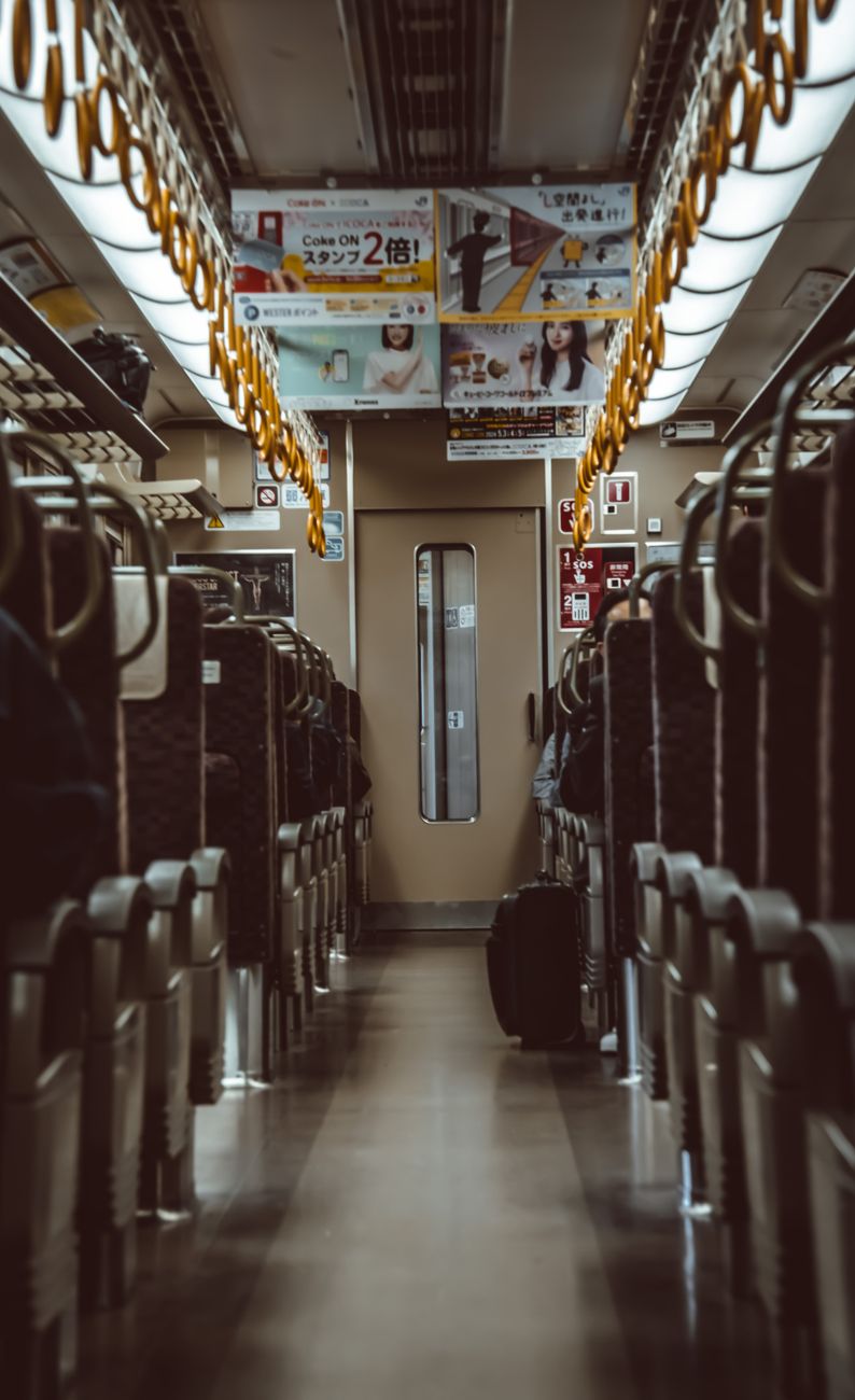 Elderly passenger seated in designated priority seat area marked with pink upholstery near Japanese train door.