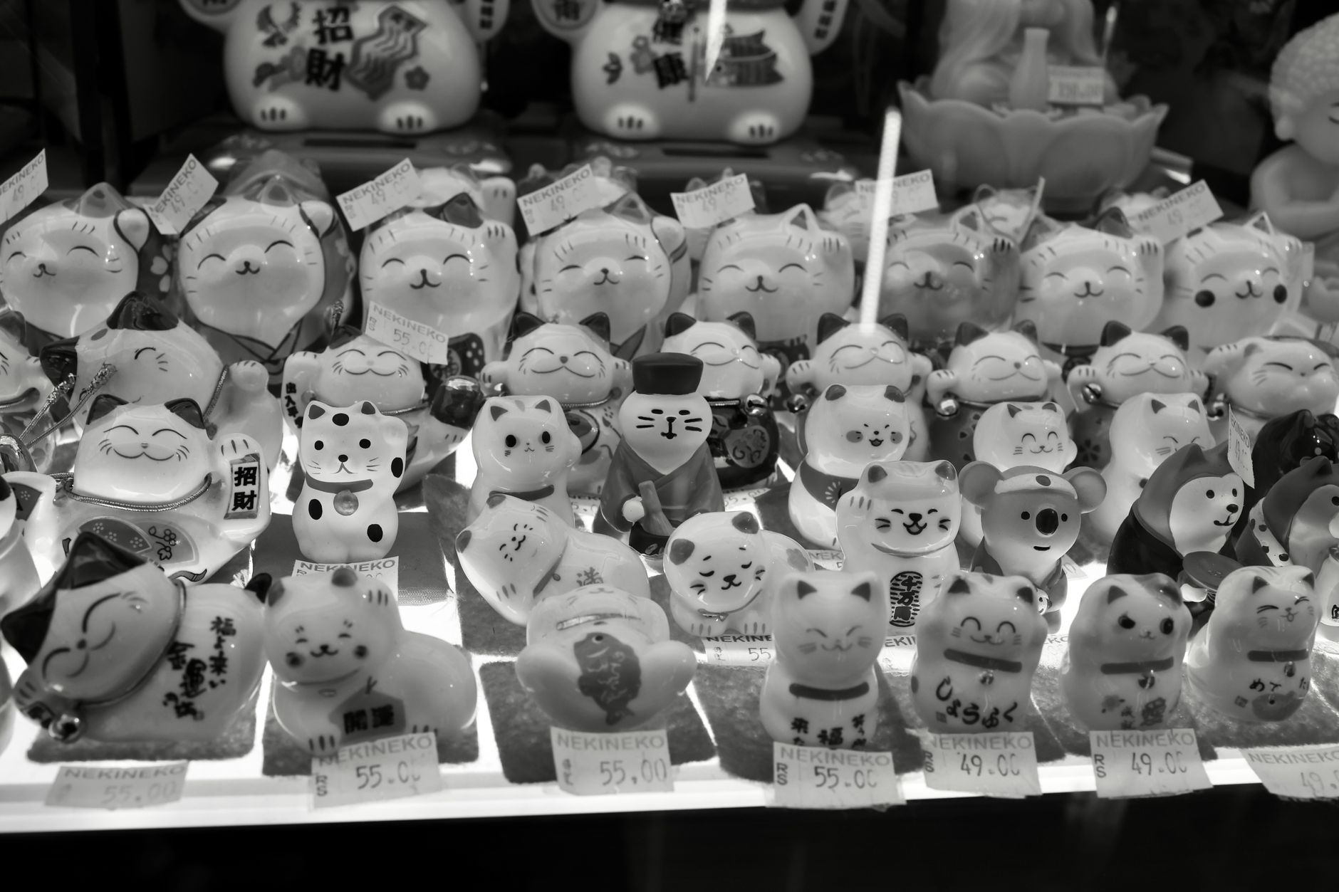 White ceramic maneki neko figurine with raised left paw and red collar sitting beside a shop entrance in Japan.