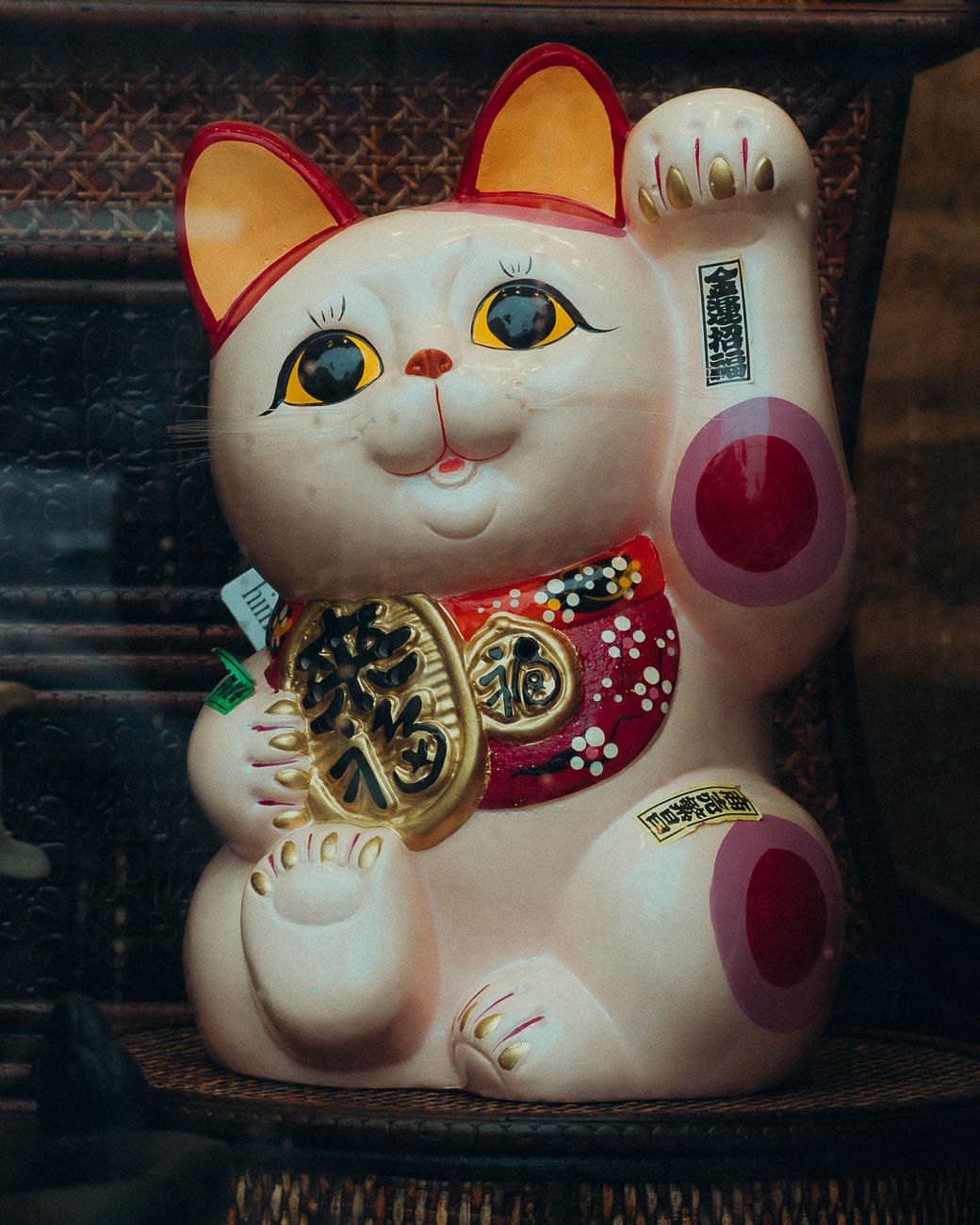 White ceramic maneki neko figurine with raised left paw and red collar sitting beside a shop entrance in Japan.