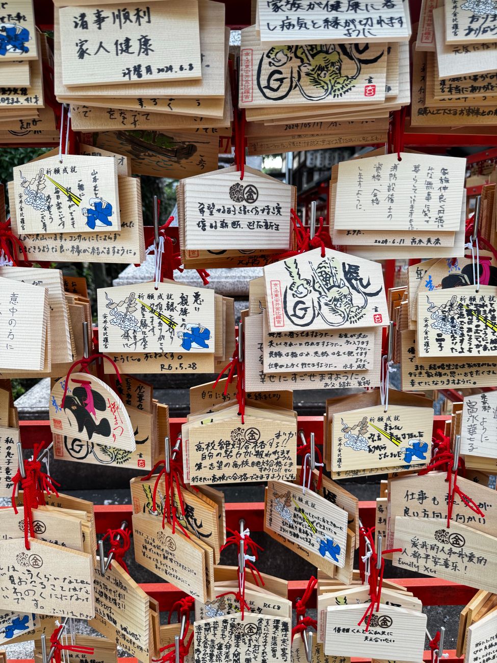 Colorful wooden ema plaques hanging at a Japanese shrine, displaying handwritten wishes and prayers in black ink.
