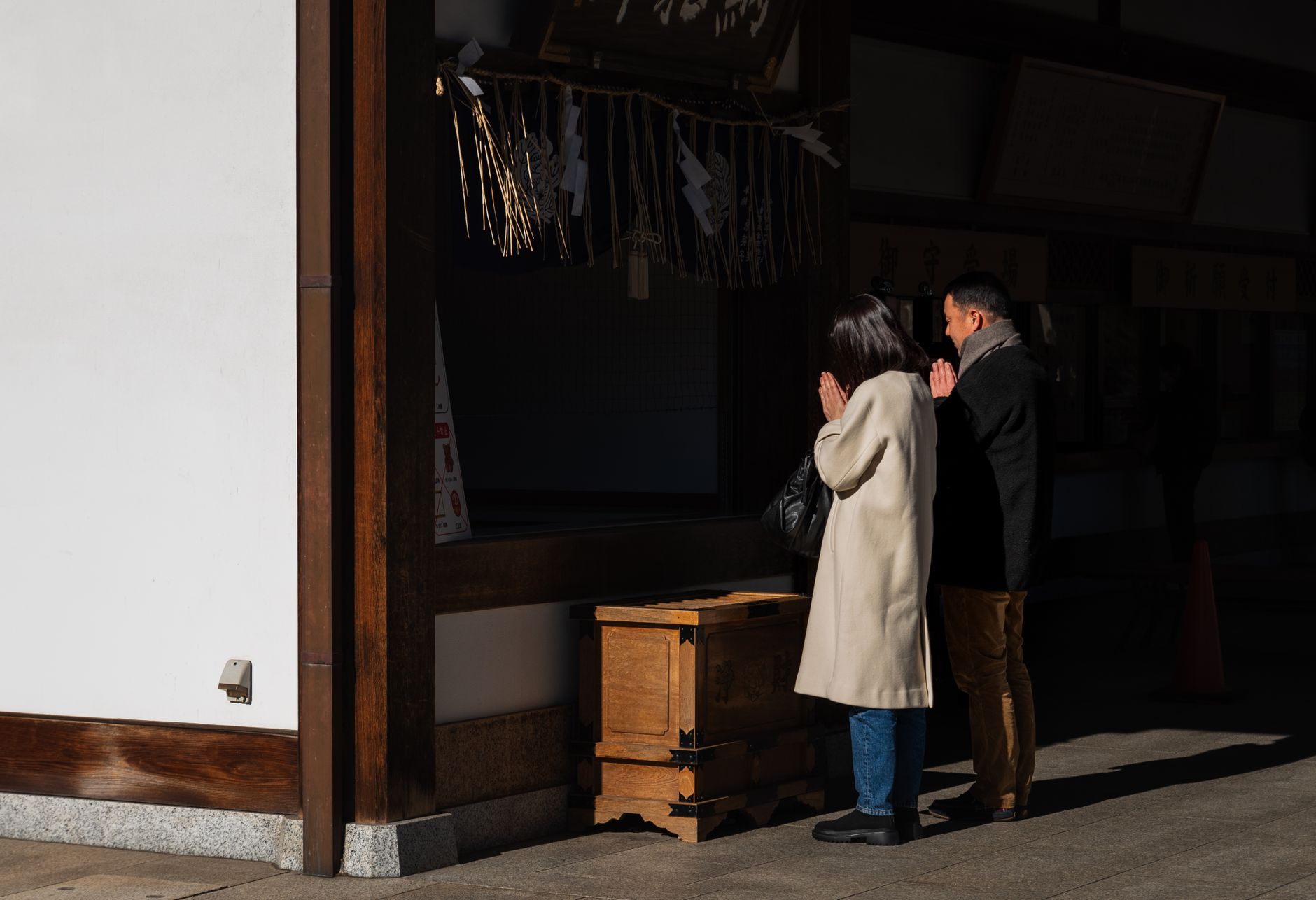 Small fabric omamori charm pouches in red, white, and gold hanging from wooden display at Japanese shrine.