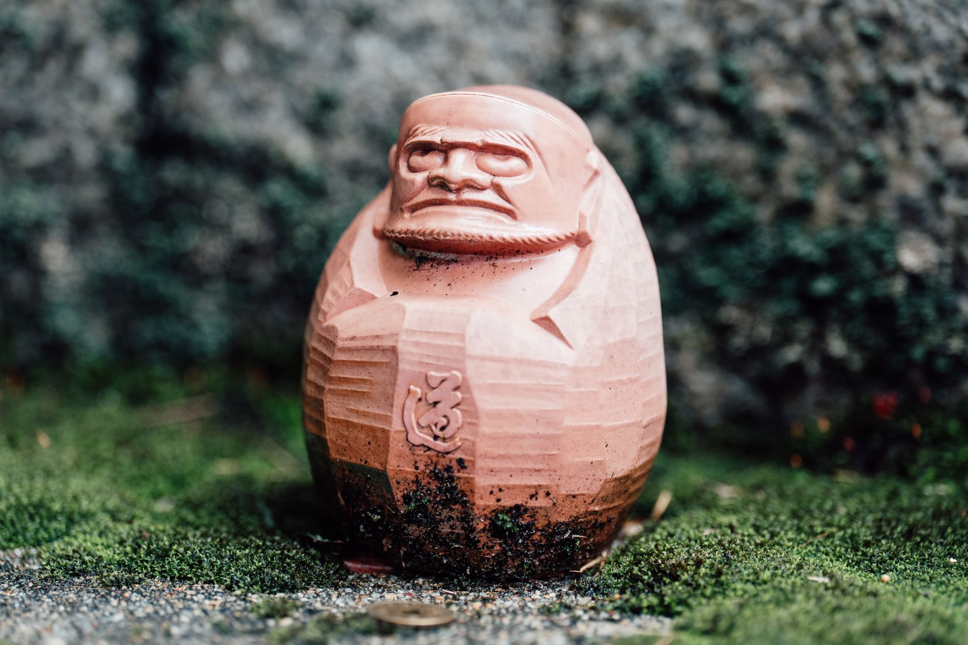 Round red Daruma doll with blank white eyes and gold details sitting on a wooden shelf in a traditional Japanese home.