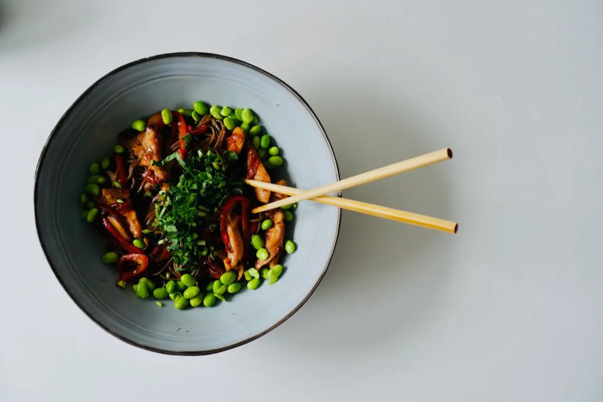 Steaming buckwheat soba noodles served in a traditional ceramic bowl with garnishes on a wooden table.