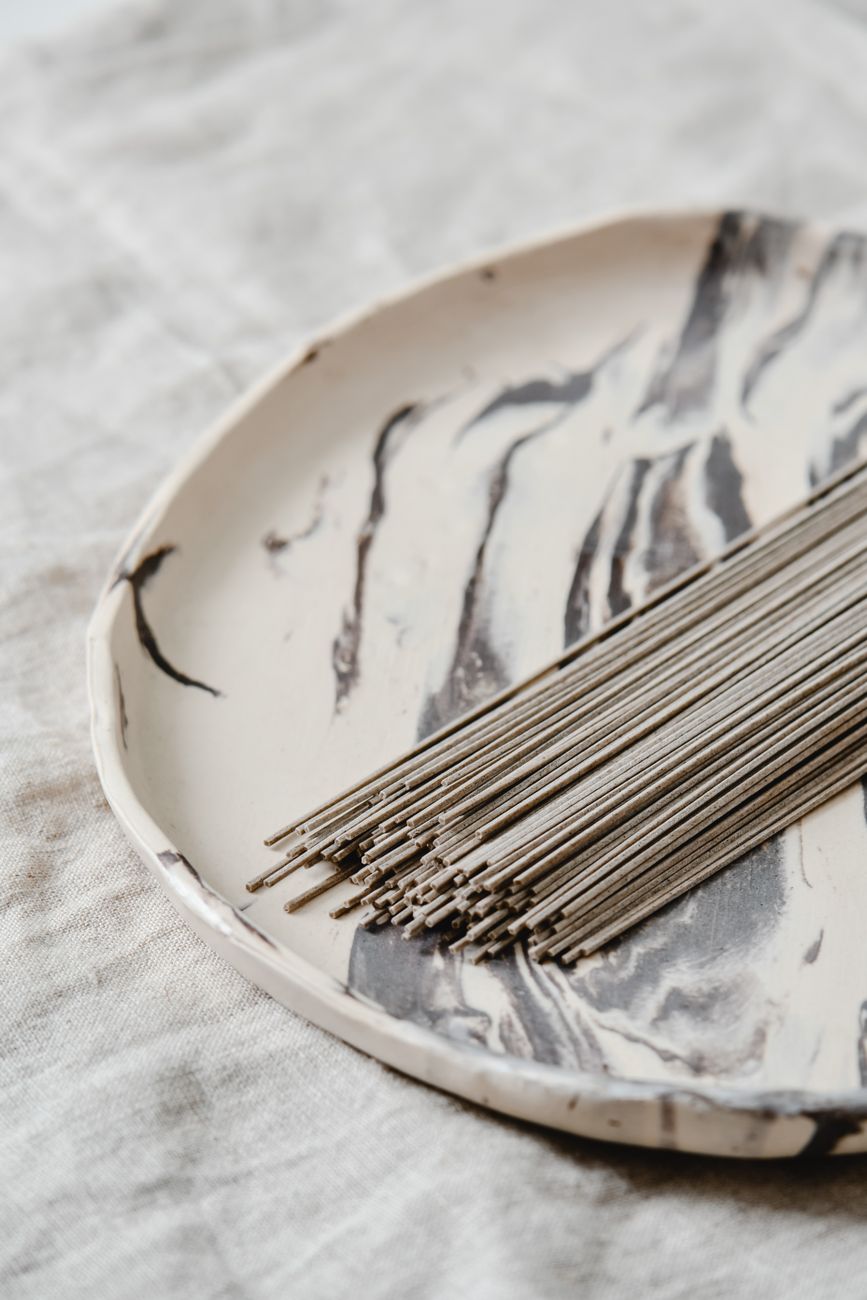 Steaming buckwheat soba noodles served in a traditional ceramic bowl with garnishes on a wooden table.