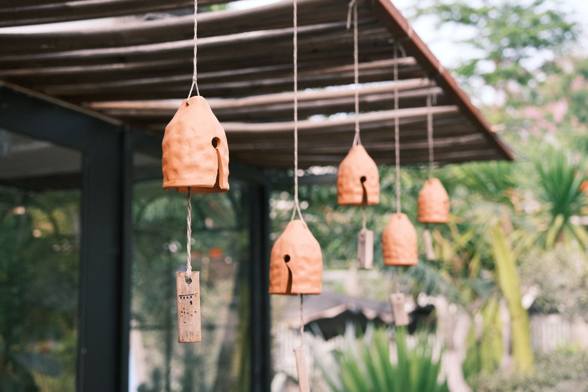 Glass wind chime hanging from Japanese house eave with paper strip swaying in summer breeze against blue sky.