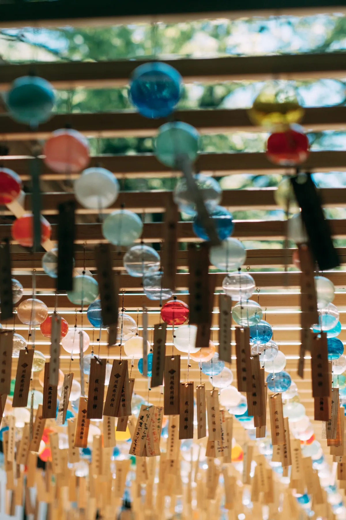 Glass wind chime hanging from Japanese house eave with paper strip swaying in summer breeze against blue sky.