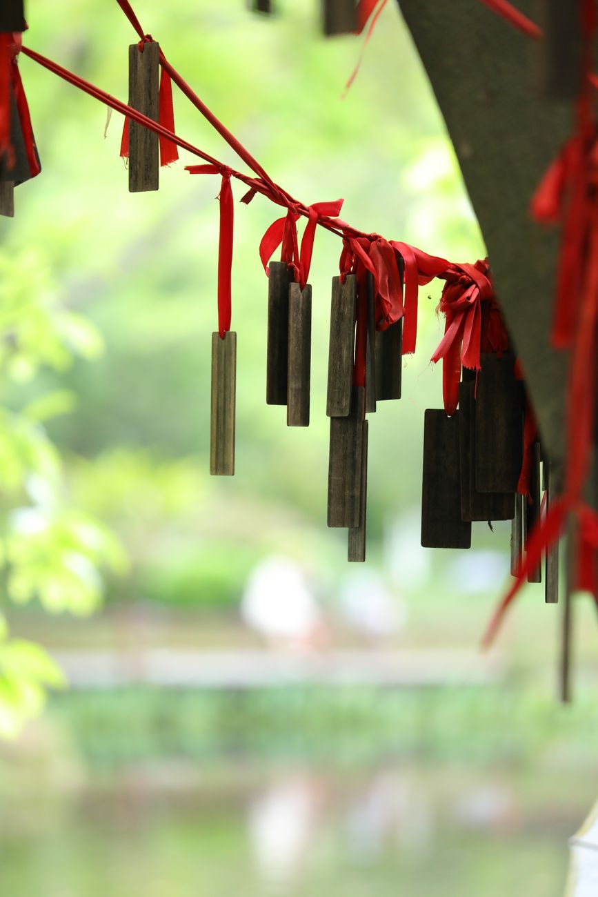 Glass wind chime hanging from Japanese house eave with paper strip swaying in summer breeze against blue sky.