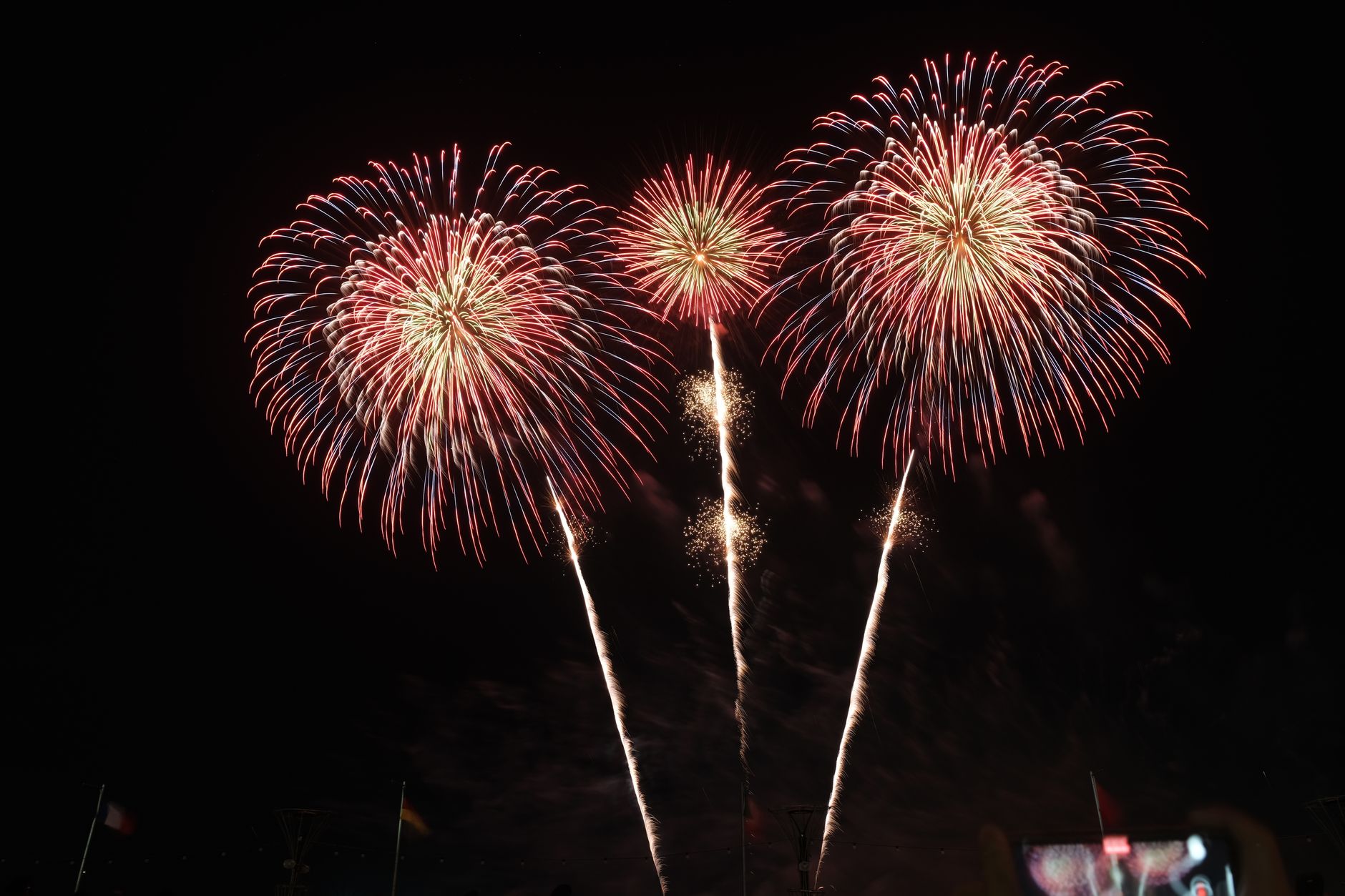 Colorful fireworks bursting over a Japanese riverside at dusk as crowds in yukata gather on blankets to watch the summer display.