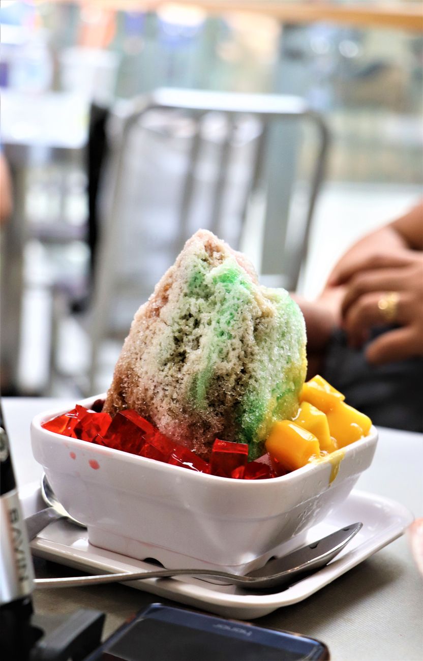 Bowl of colorful kakigori topped with sweet syrup and condensed milk, served on a wooden tray at a traditional Japanese summer festival.