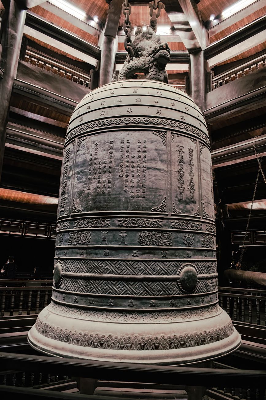 Large bronze temple bell hanging from wooden frame with thick rope, ready to be struck during Japanese New Year ceremony.