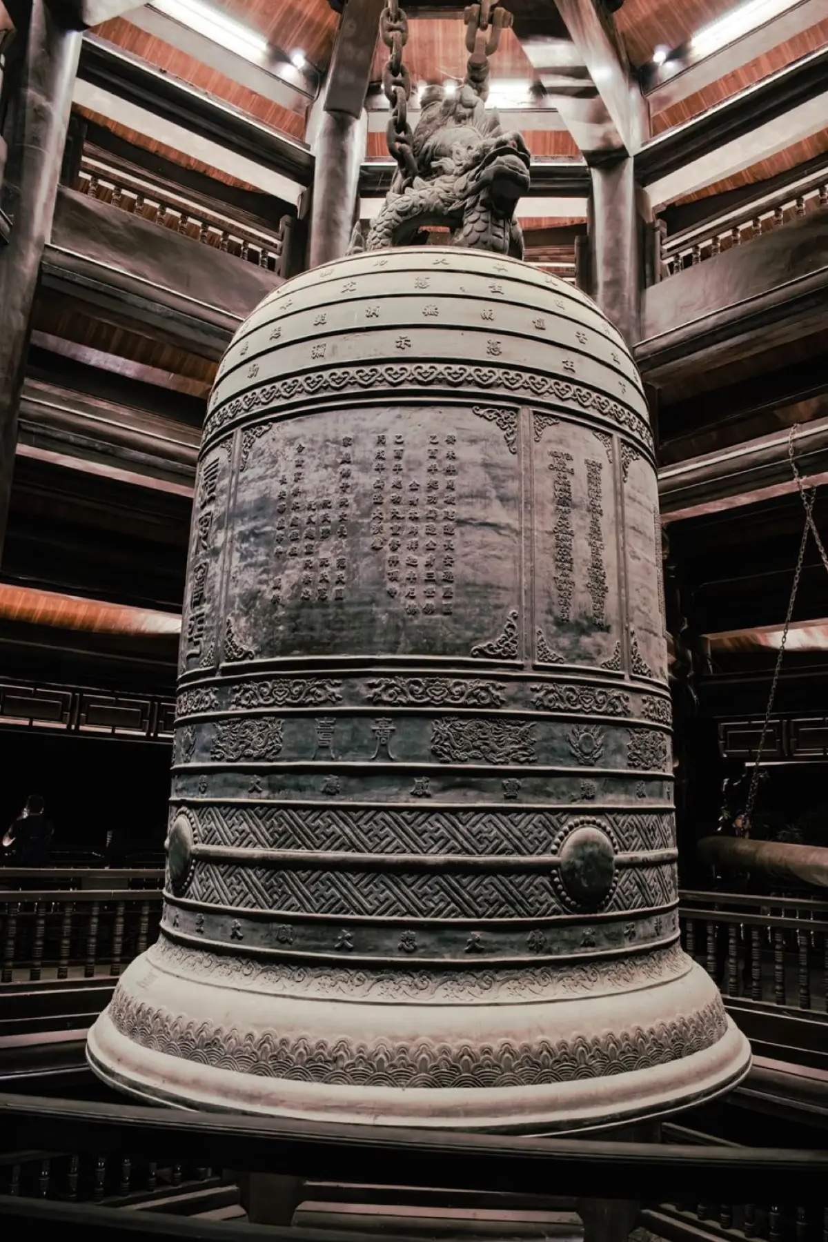 Large bronze temple bell hanging from wooden frame with thick rope, ready to be struck during Japanese New Year ceremony.