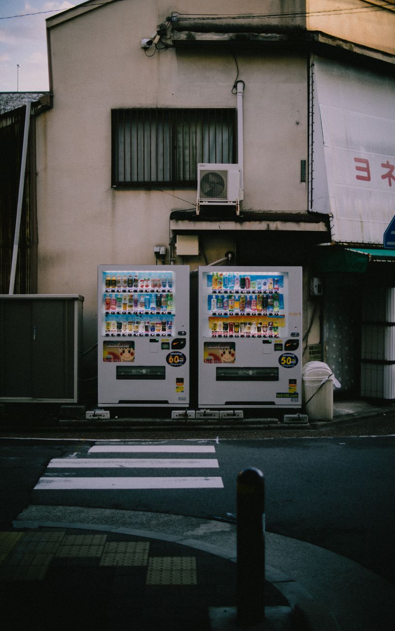 Rows of illuminated vending machines displaying colorful drinks line a quiet Tokyo street at night with bicycles parked nearby.