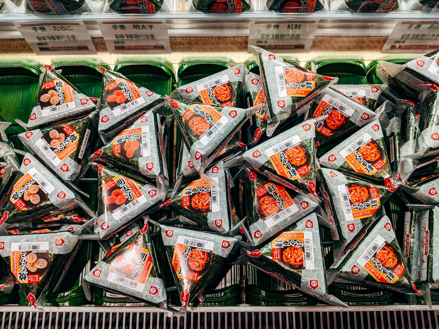 Colorful displays of Japanese sweets, bento boxes, and fresh produce arranged in pristine glass cases at a bustling department store basement.
