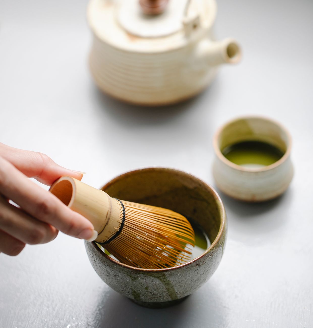 Vibrant green matcha powder whisked into foam inside a traditional ceramic tea bowl with bamboo chasen whisk nearby.