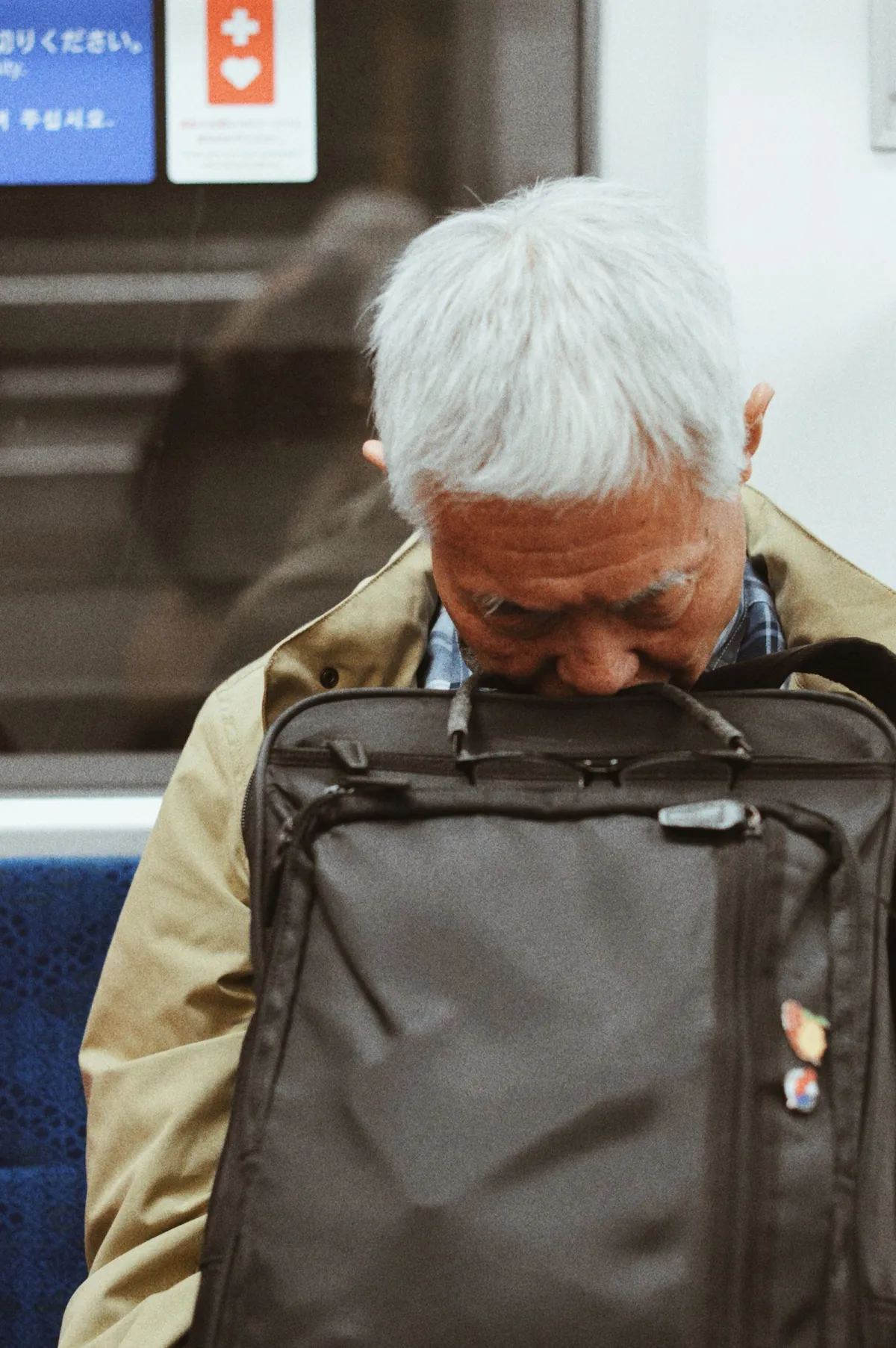 Japanese businessman in suit sleeping upright on train seat during morning commute, head tilted back with briefcase on lap.