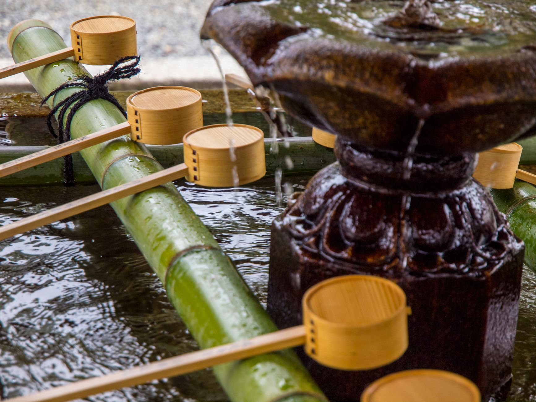 Visitors using long-handled ladles to rinse hands at a traditional stone water basin outside a Japanese shrine entrance.