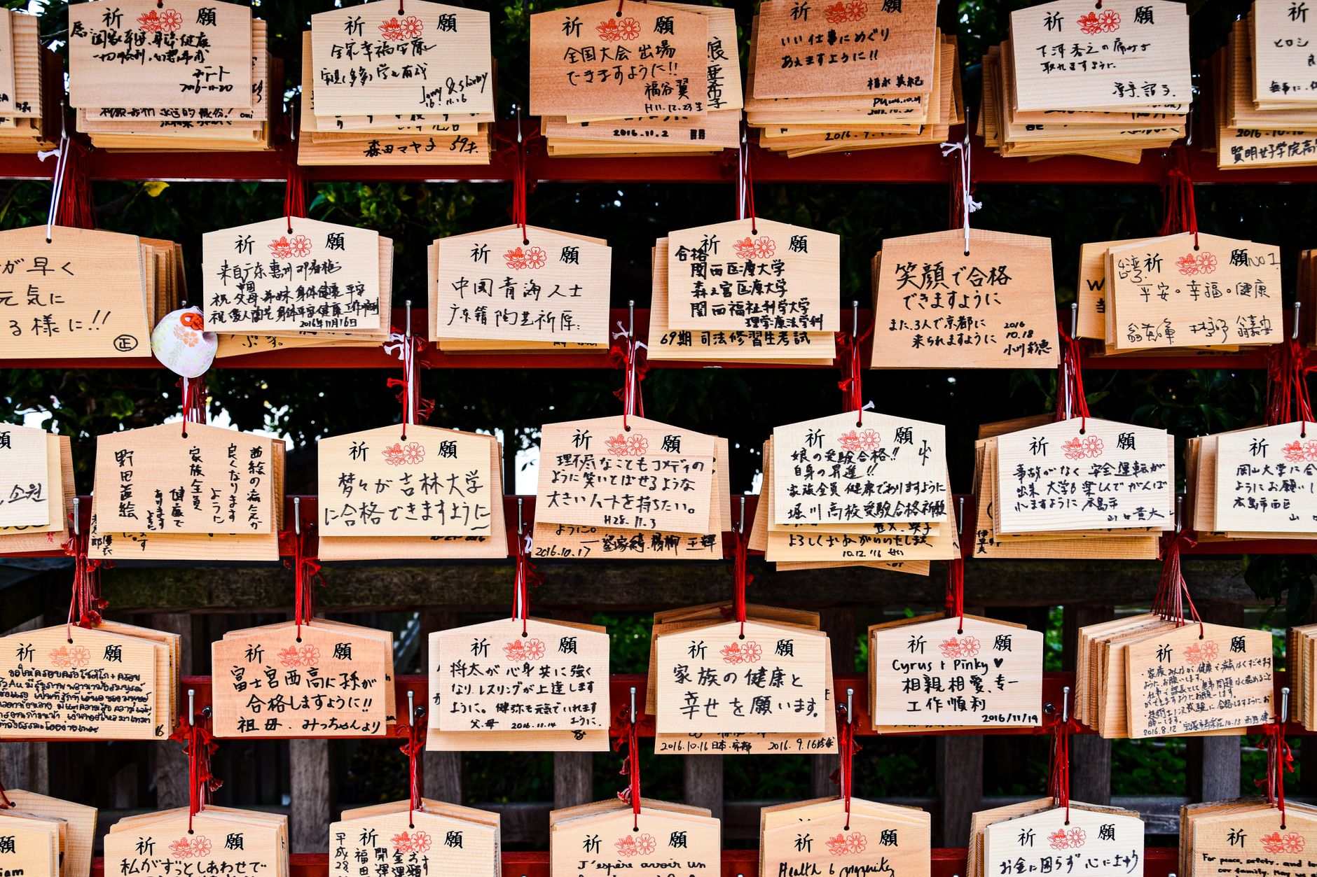 Colorful wooden ema plaques hanging at a Japanese shrine displaying handwritten wishes and prayers in black ink.