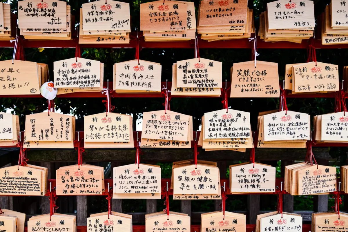 Colorful wooden ema plaques hanging at a Japanese shrine displaying handwritten wishes and prayers in black ink.