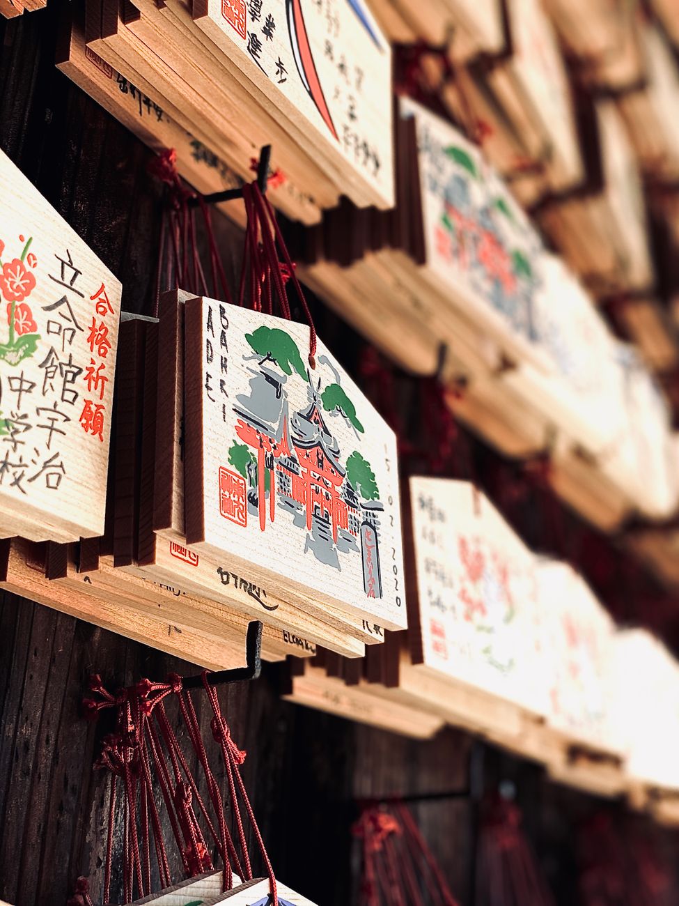 Colorful wooden ema plaques hanging at a Japanese shrine displaying handwritten wishes and prayers in black ink.