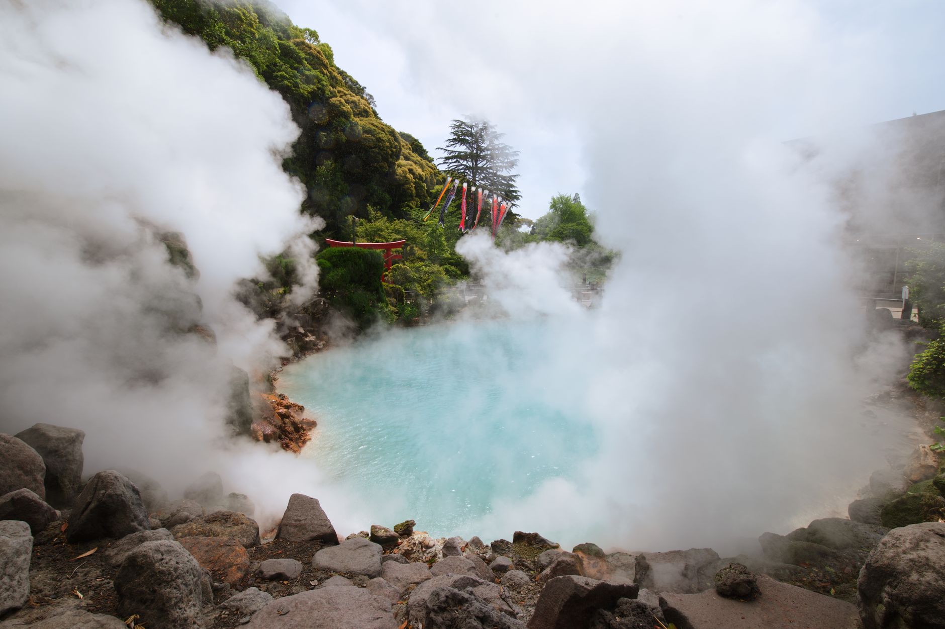 Traditional Japanese outdoor hot spring bath surrounded by natural rocks and steam rising into mountain forest scenery at dawn.