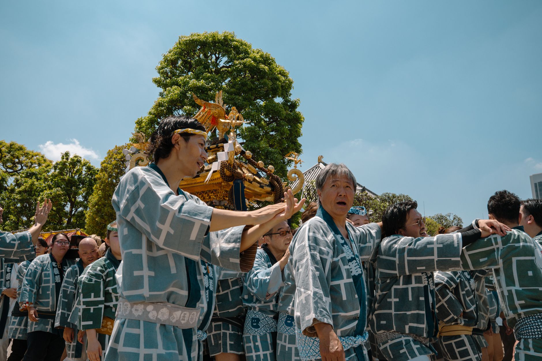 Festival participants in traditional happi coats carrying an ornate golden mikoshi shrine through crowded streets during a Japanese matsuri celebration.
