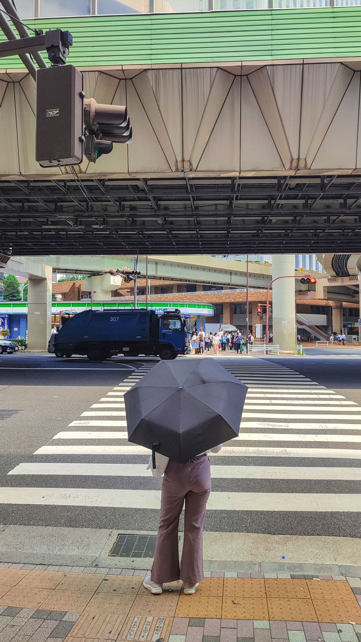 Transparent plastic sleeve covering a wet umbrella standing in a holder at a Japanese store entrance on a rainy day.