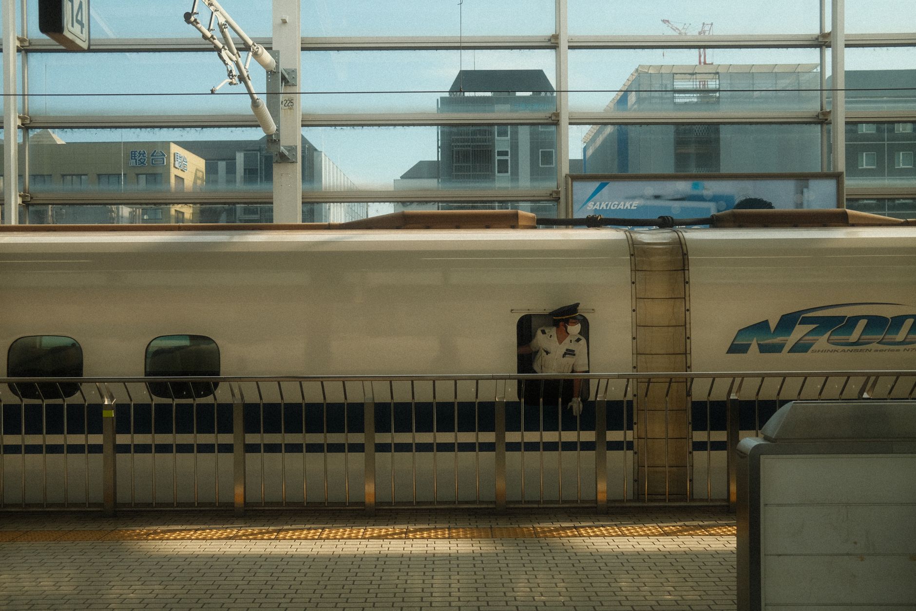 Japanese train conductor in navy uniform pointing at platform sign while wearing crisp white gloves at Tokyo station.