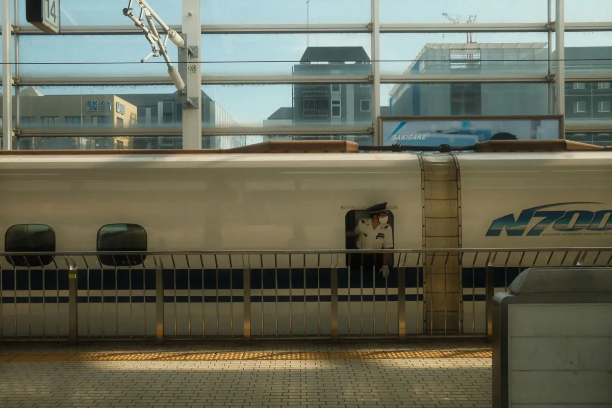 Japanese train conductor in navy uniform pointing at platform sign while wearing crisp white gloves at Tokyo station.