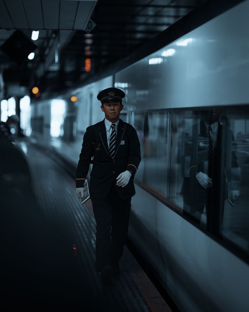 Japanese train conductor in navy uniform pointing at platform sign while wearing crisp white gloves at Tokyo station.