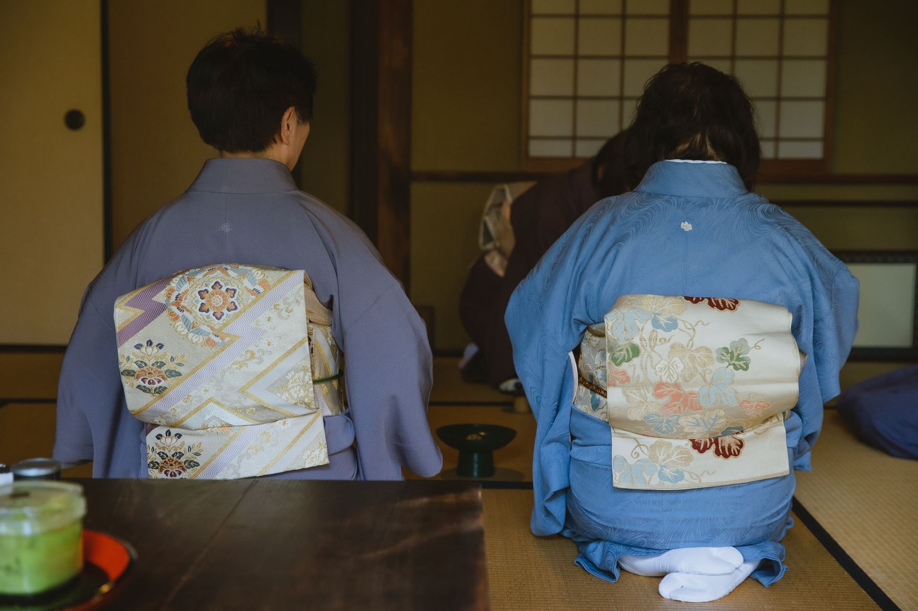 Stone grinding wheel producing vibrant green matcha powder in a traditional Japanese tea house with wooden architecture.