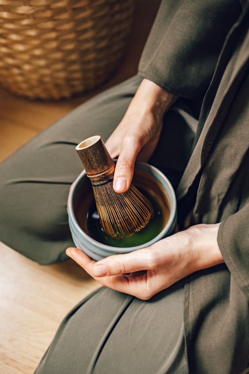 Stone grinding wheel producing vibrant green matcha powder in a traditional Japanese tea house with wooden architecture.