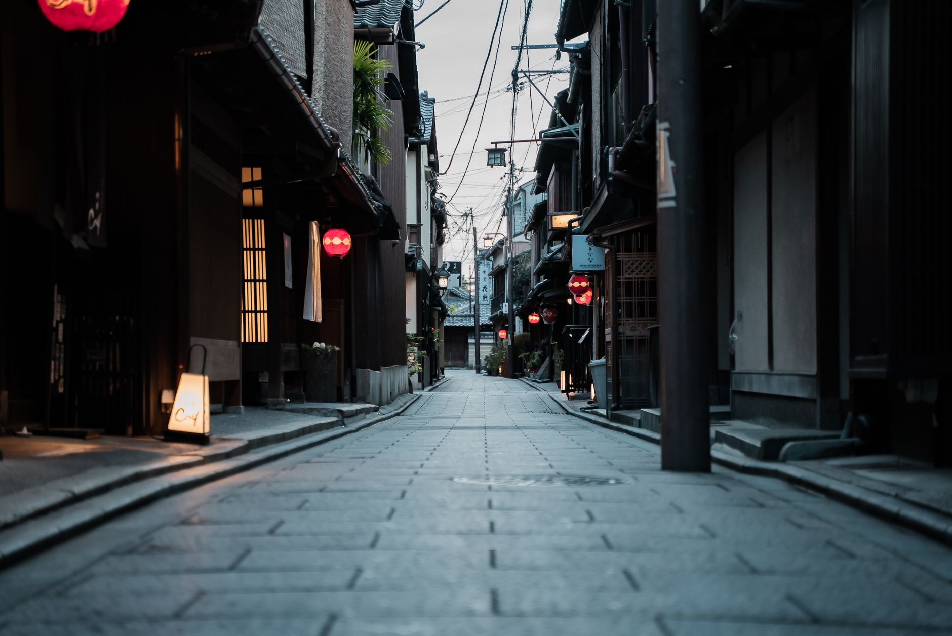 Traditional wooden Kyoto machiya townhouse with narrow frontage, latticed windows, and dark timber facade along a historic stone-paved street.