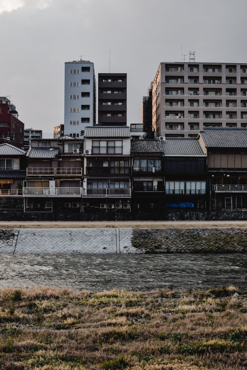 Traditional wooden Kyoto machiya townhouse with narrow frontage, latticed windows, and dark timber facade along a historic stone-paved street.