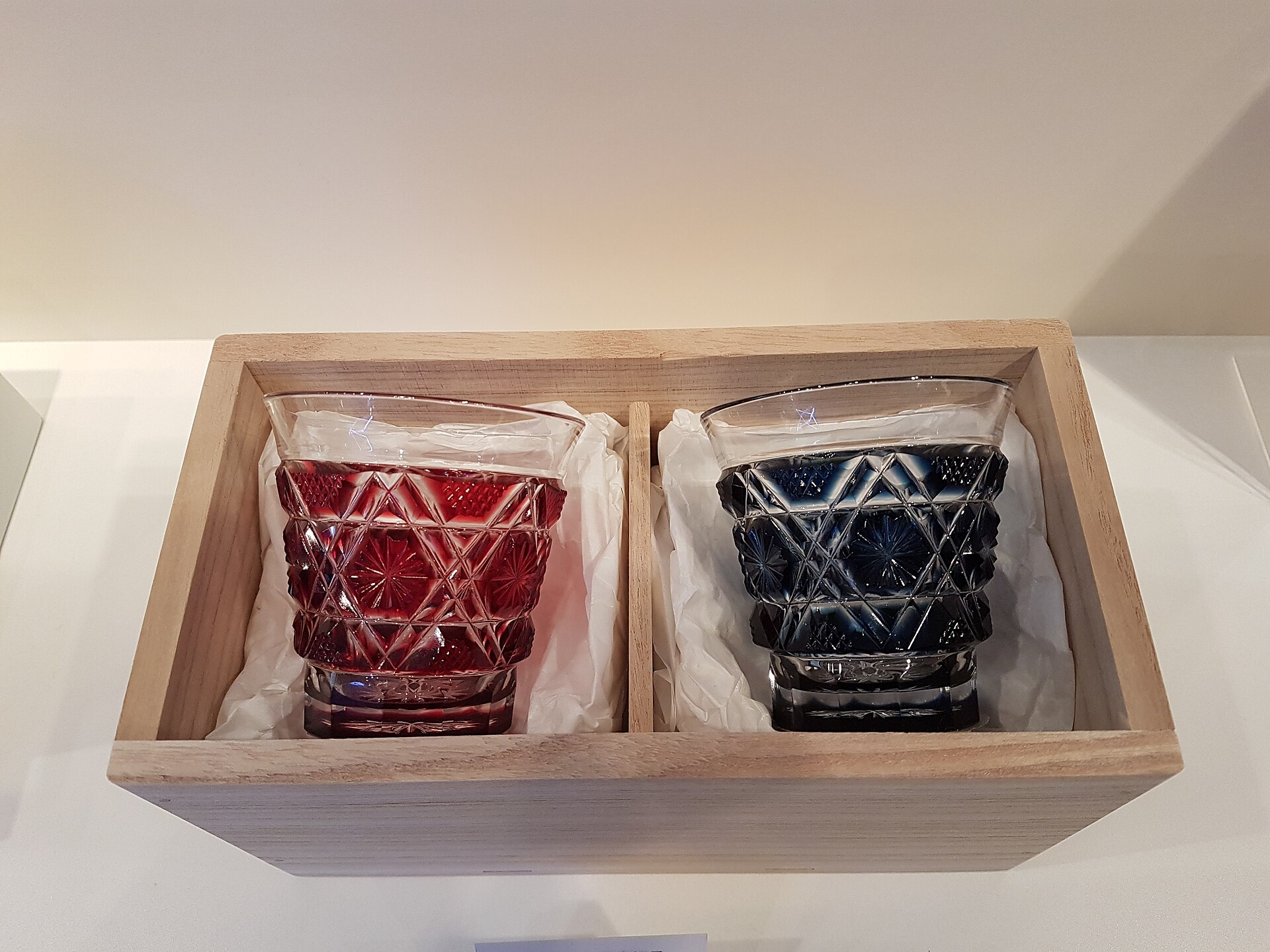 Deep crimson and cobalt blue Satsuma Kiriko cut glass vessel displaying intricate geometric patterns against soft natural light.