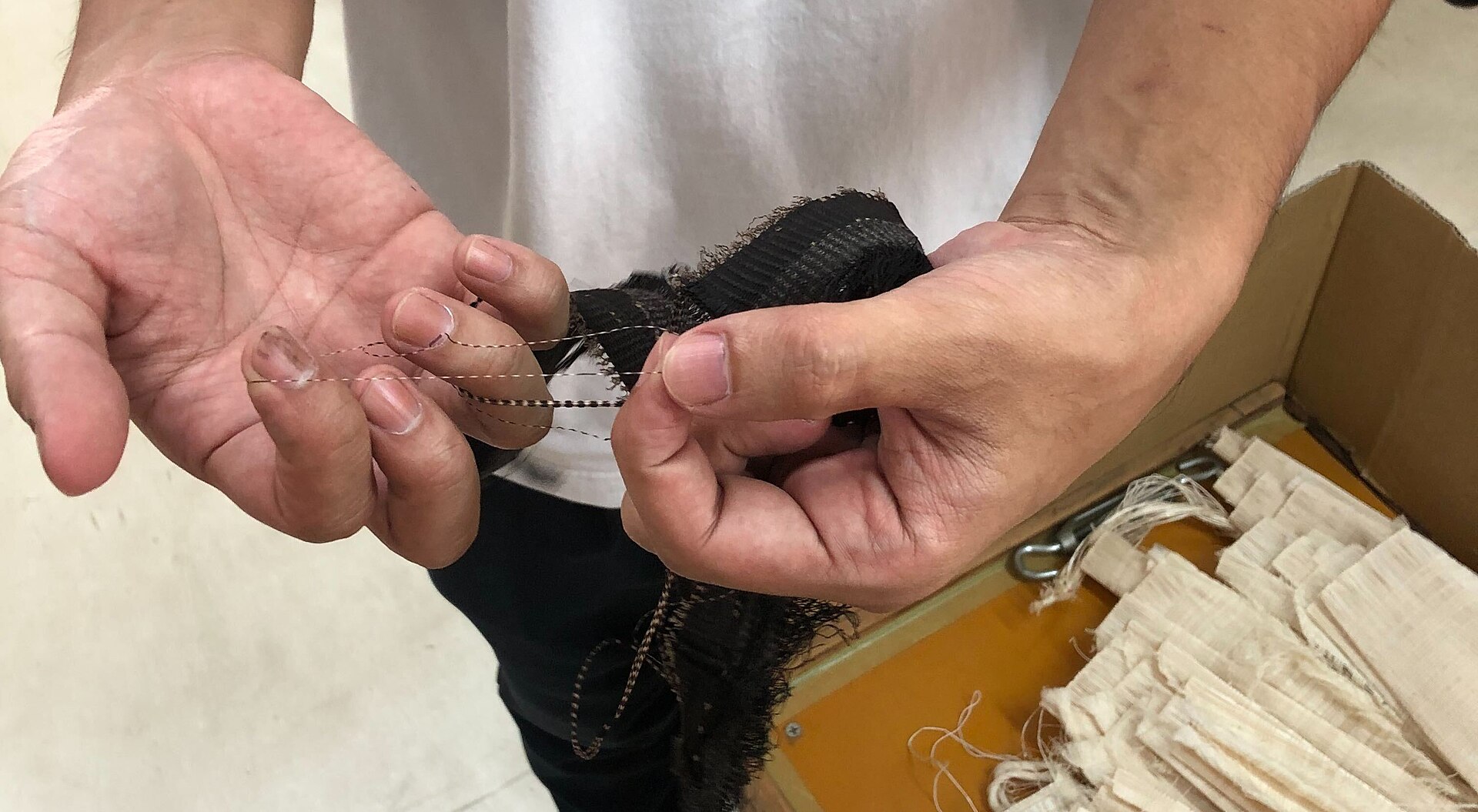 Artisan's hands dipping silk threads into iron-rich mud bath during traditional Oshima Tsumugi dyeing process in Amami.