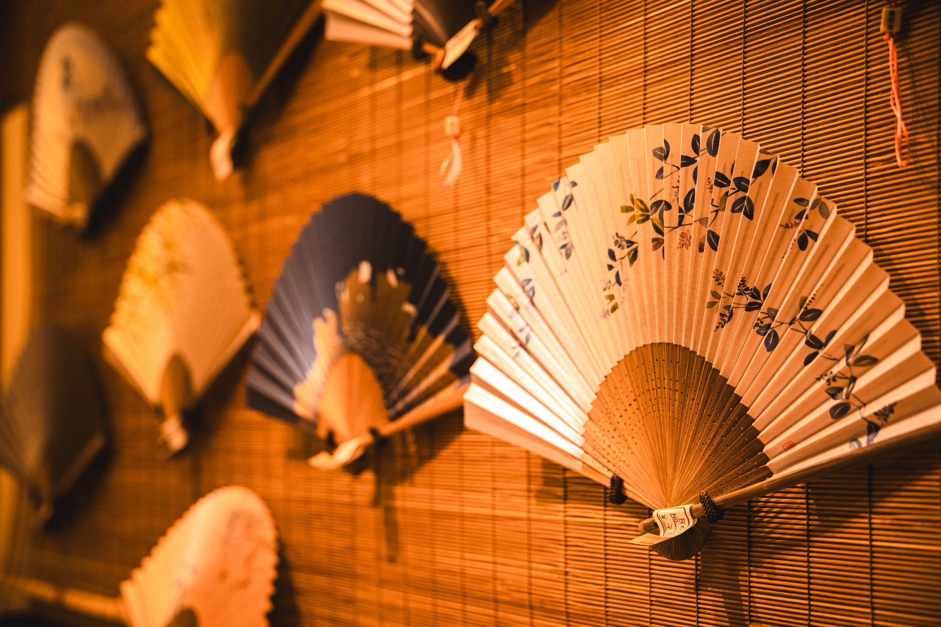 Artisan's hands applying colorful washi paper to bamboo frame of traditional Marugame uchiwa fan in workshop.