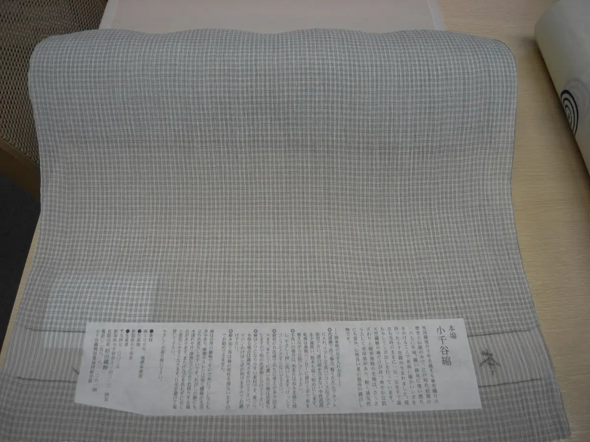 Artisan's hands weaving fine ramie threads on a traditional wooden loom, creating the distinctive crinkled texture of Ojiya chijimi fabric.