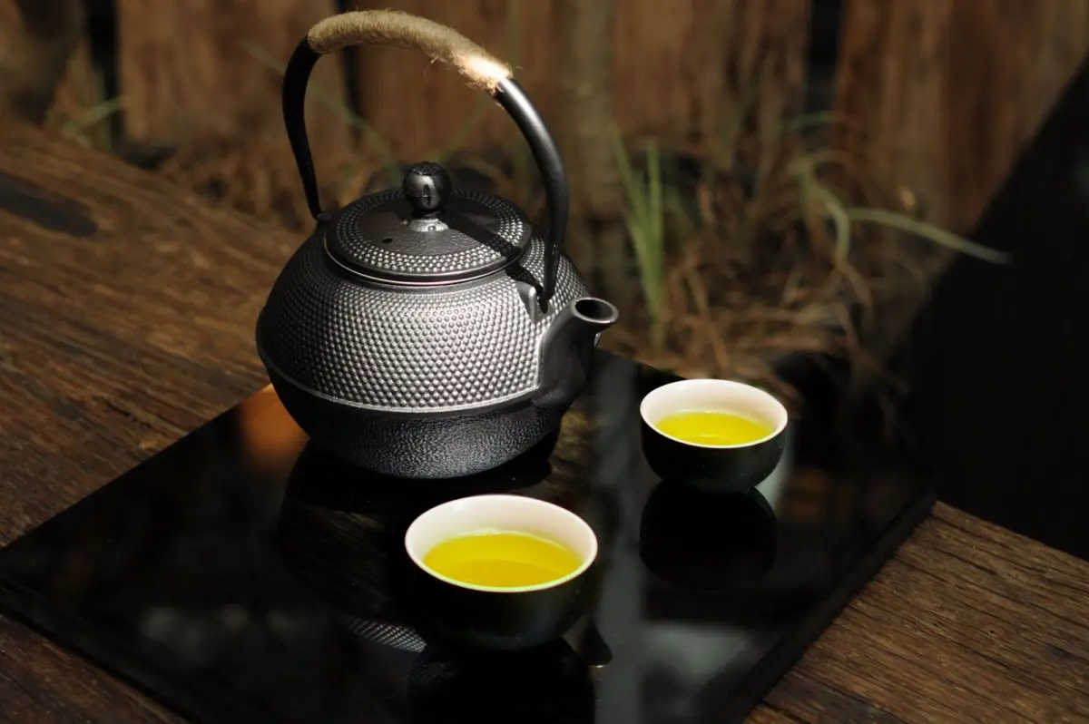 Traditional Yamagata cast iron kettle with thin walls and textured black surface, steam rising from spout during tea preparation.