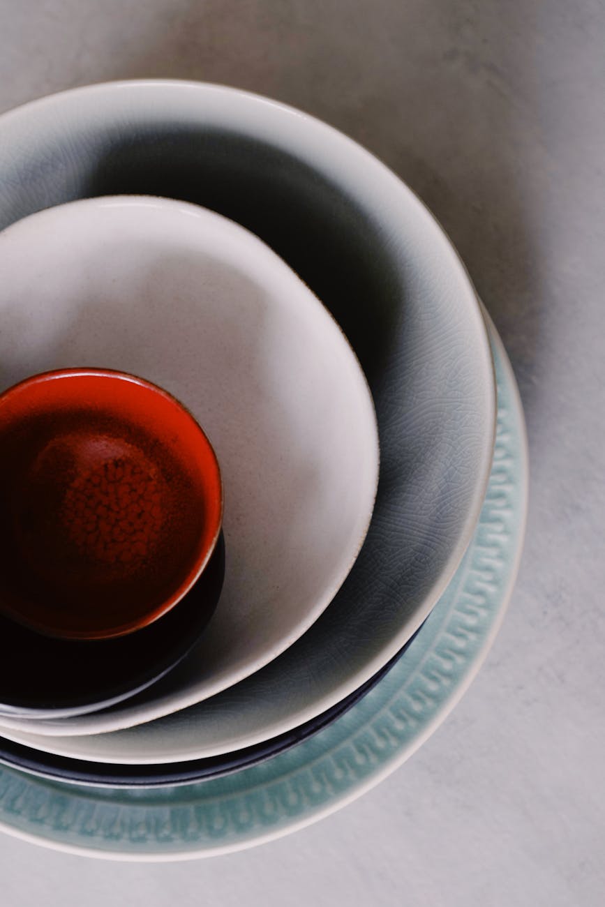Stack of simple white Hasami ware plates and bowls arranged on a wooden table in a Japanese home kitchen.