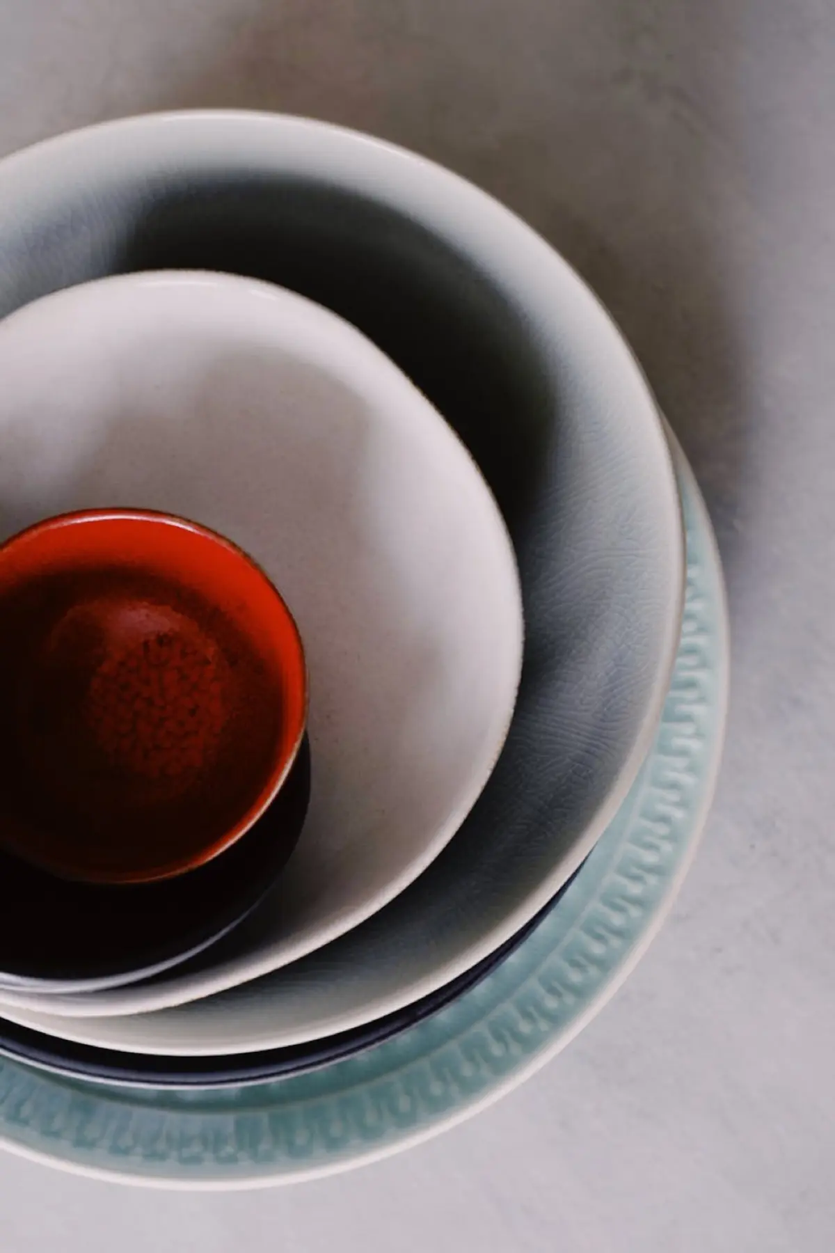 Stack of simple white Hasami ware plates and bowls arranged on a wooden table in a Japanese home kitchen.