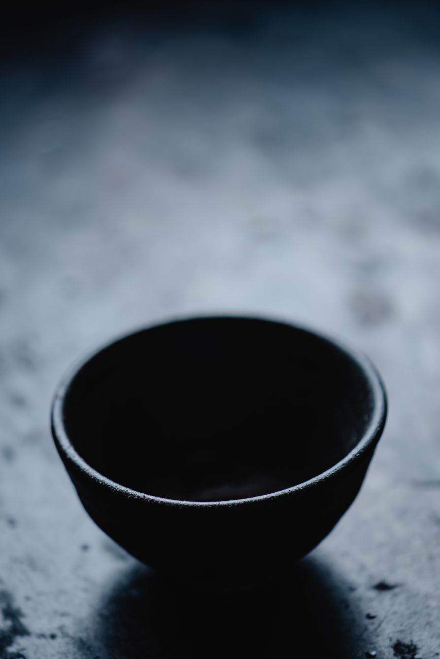 Close-up of tenmoku glazed tea bowl showing iridescent oil-spot pattern and iron-rich black surface with brown rim.