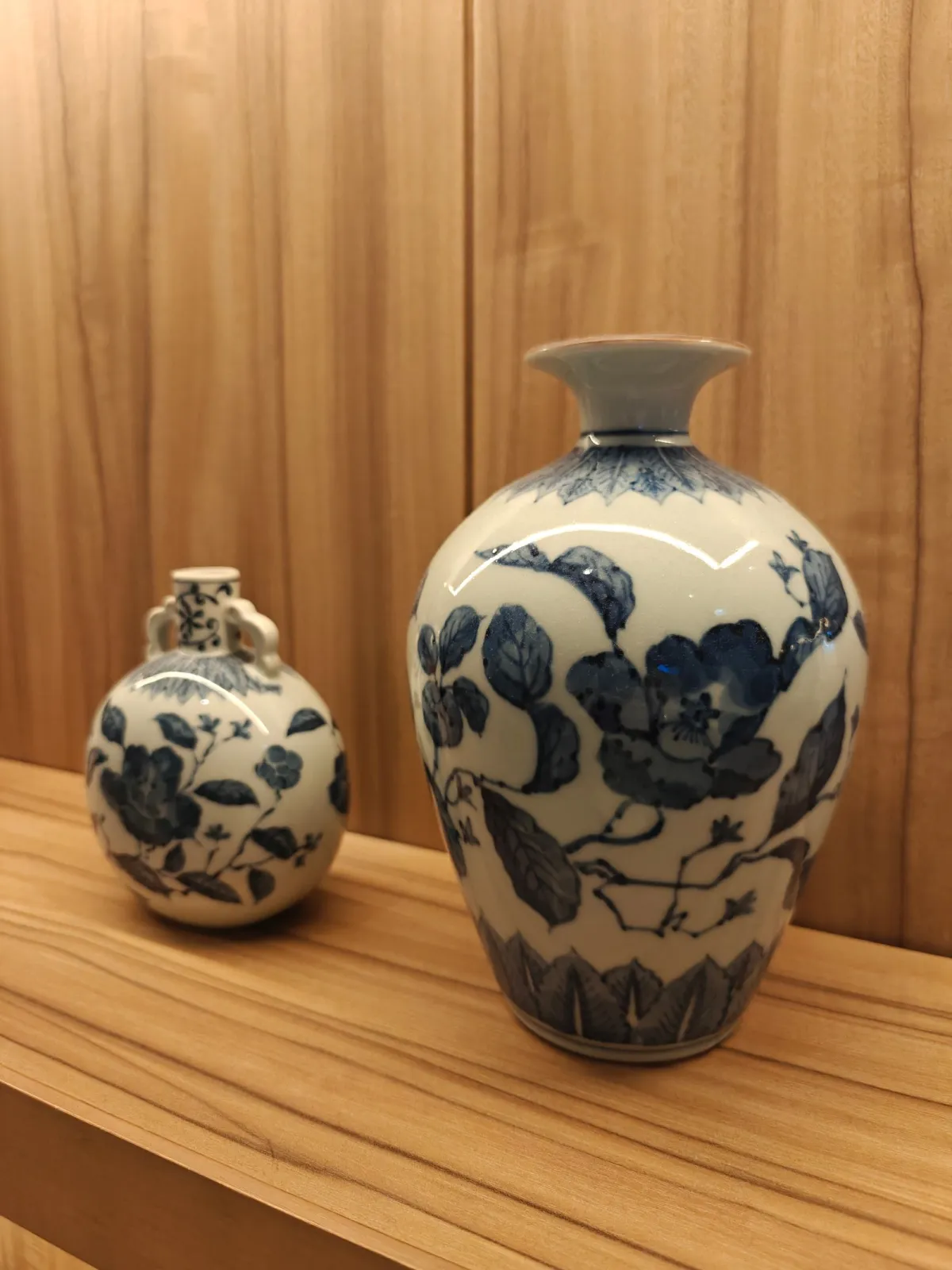 Artisan painting delicate floral motifs with cobalt pigment onto bisque-fired porcelain bowl using fine brush technique.