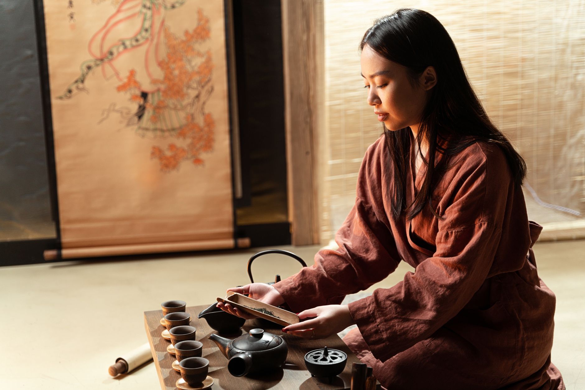 Elderly tea master in kimono performs precise hand movements while whisking matcha in black ceramic bowl during traditional ceremony.