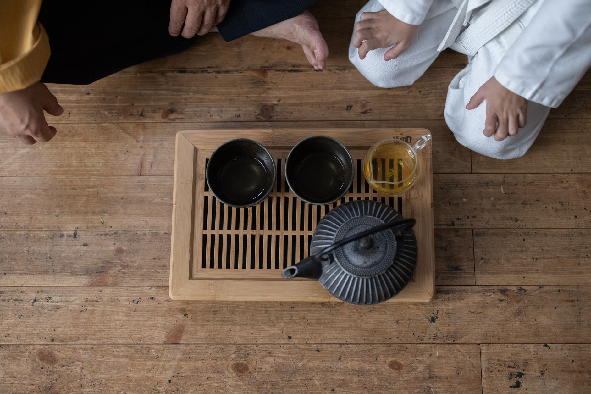 Vibrant green gyokuro tea leaves in a ceramic bowl beside a traditional Japanese teapot on bamboo mat.