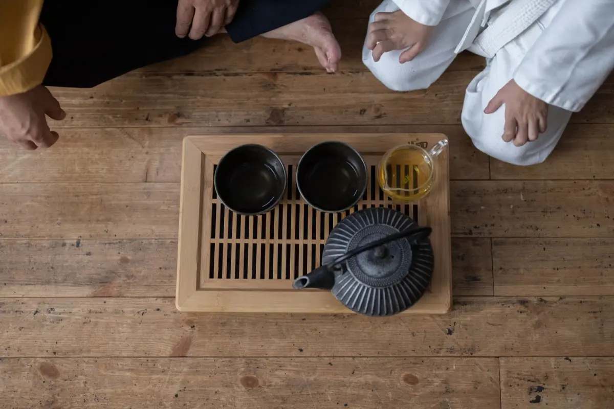 Vibrant green gyokuro tea leaves in a ceramic bowl beside a traditional Japanese teapot on bamboo mat.