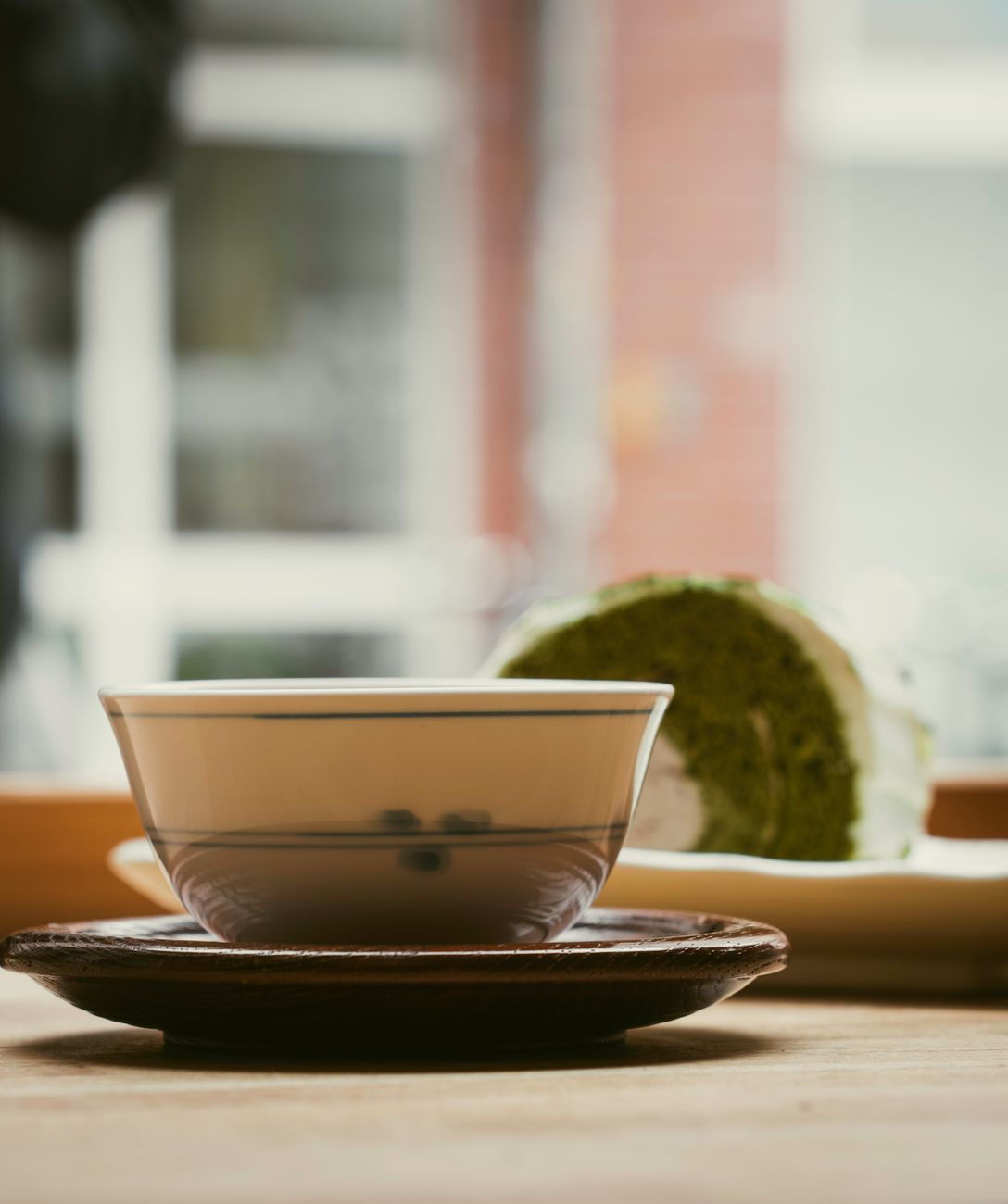 Vibrant green gyokuro tea leaves in a ceramic bowl beside a traditional Japanese teapot on bamboo mat.