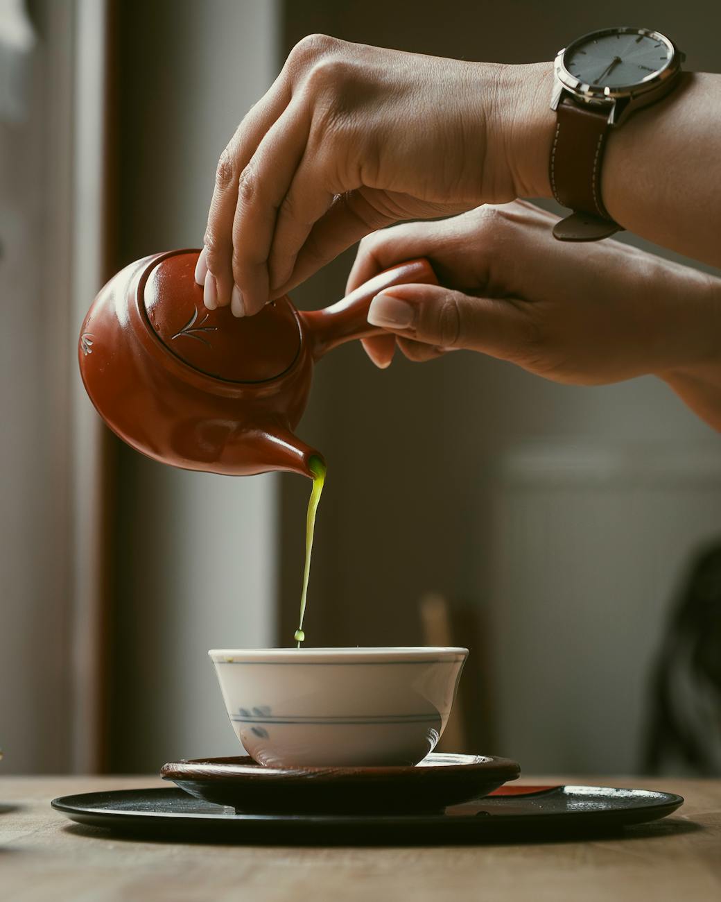 Hojicha tea leaves in warm brown tones next to a white porcelain teacup filled with amber roasted tea