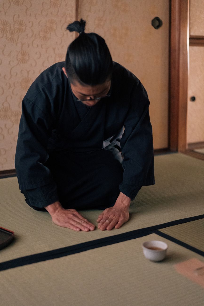 Toasted brown rice grains mixed with green tea leaves in a traditional ceramic bowl on wooden surface.