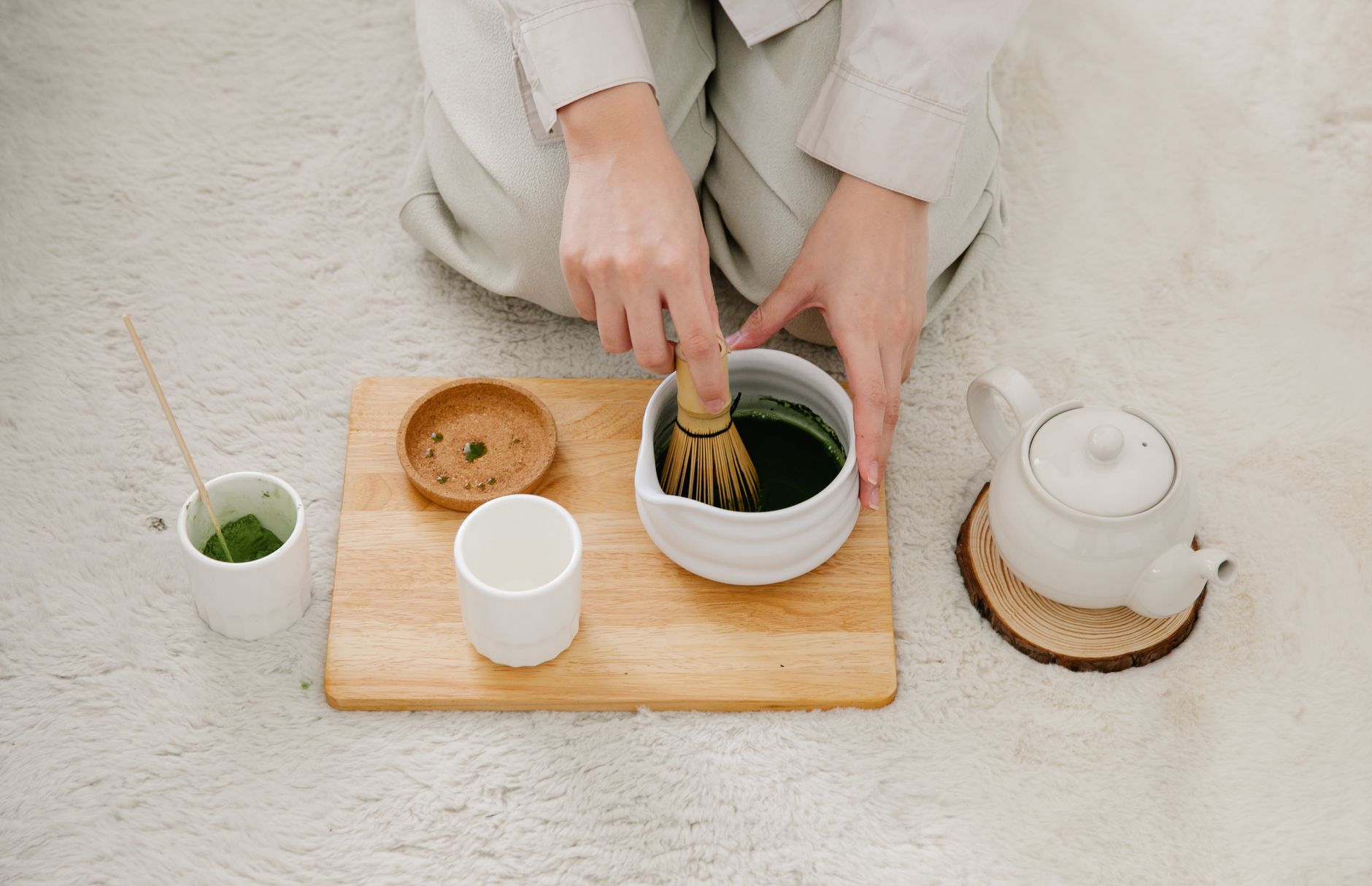 Vibrant green fukamushicha tea leaves with fine broken particles next to brewed deep-steamed sencha in a ceramic cup.