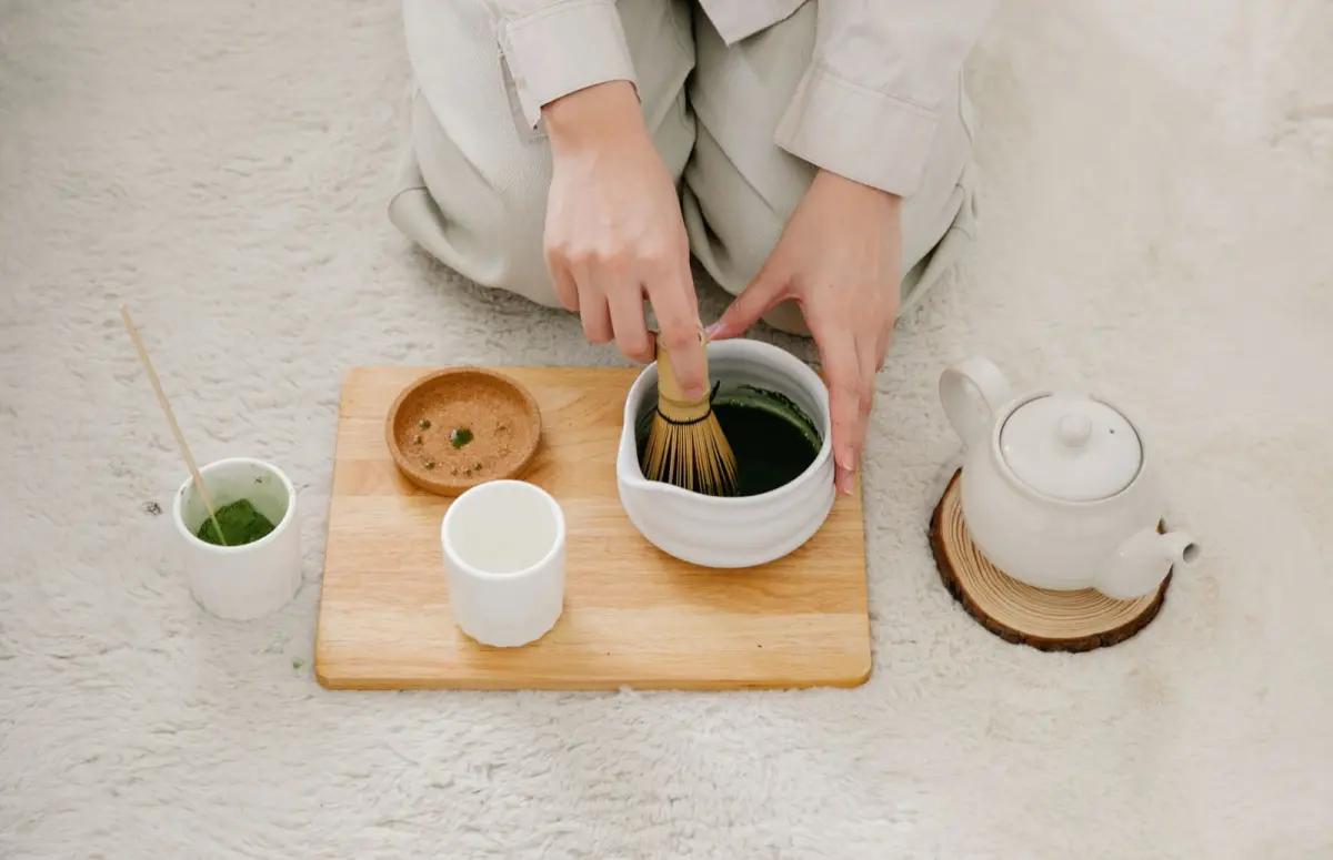 Vibrant green fukamushicha tea leaves with fine broken particles next to brewed deep-steamed sencha in a ceramic cup.